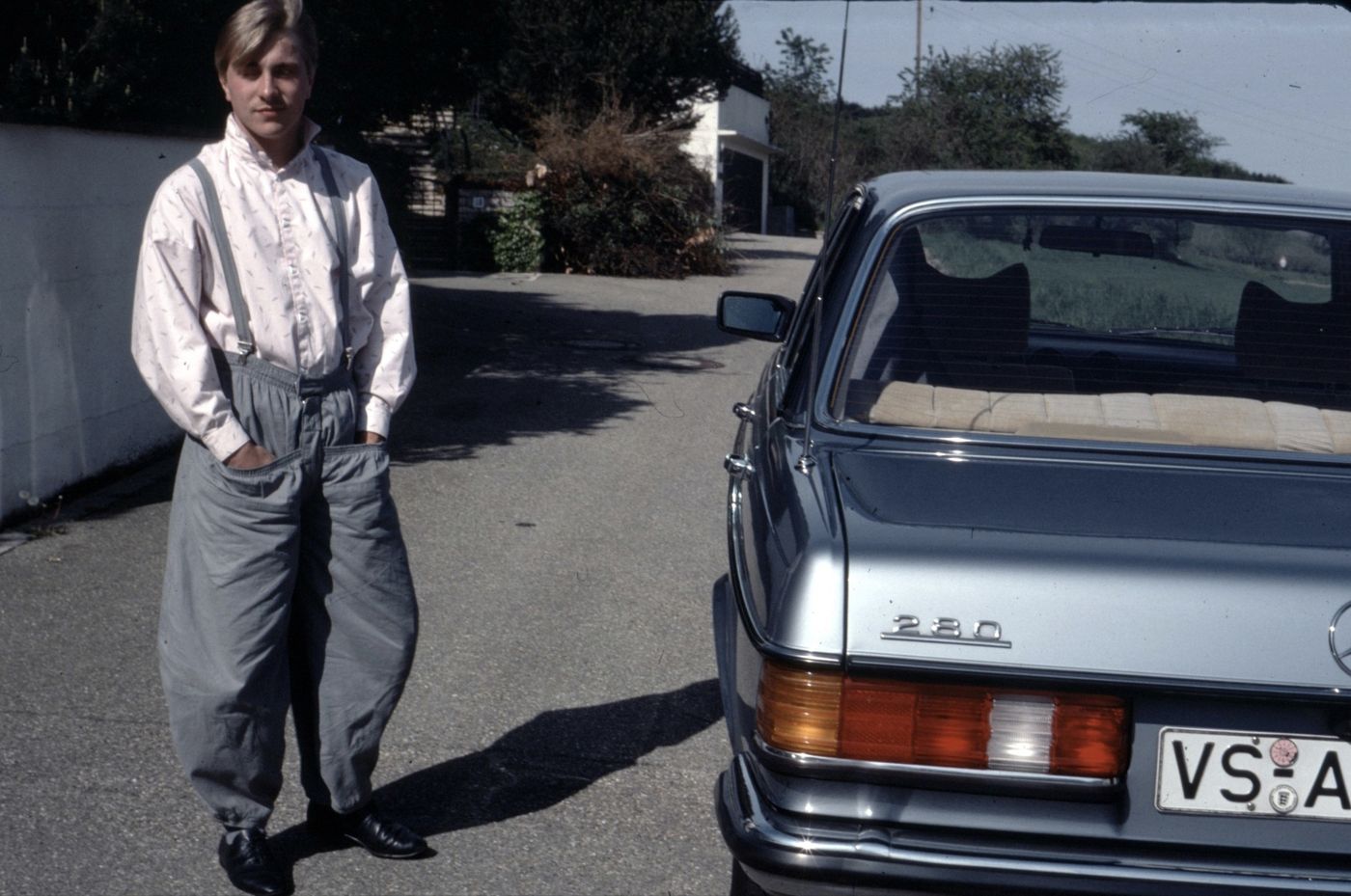 Young Patrick in self-sewn wide trousers next to a Mercedes