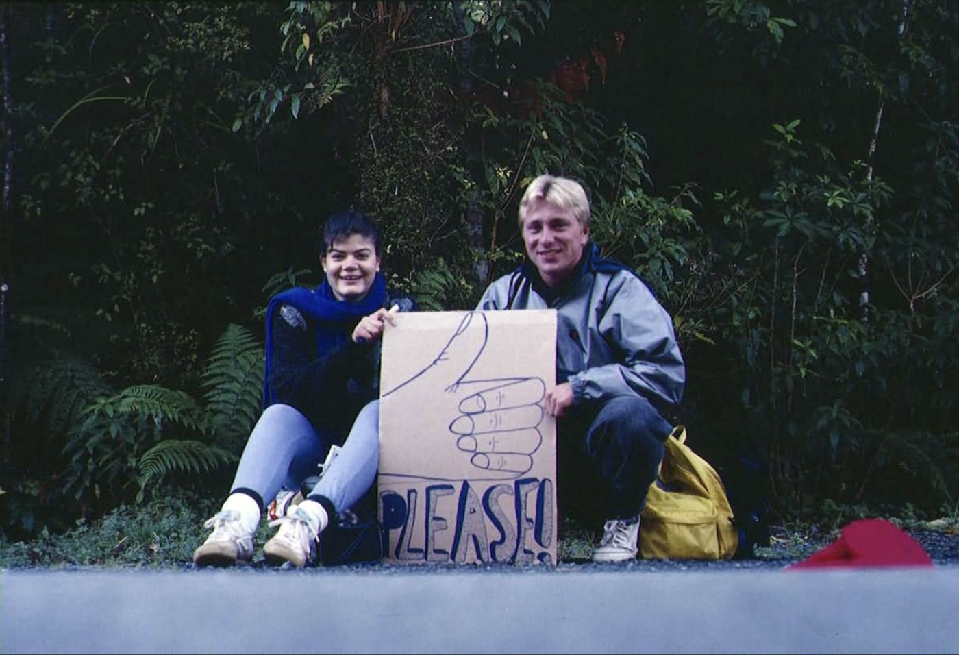 Two young travellers hitchhiking with a cardboard sign
